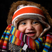A baby wearing many items of winter clothing: headband, cap, fur-lined coat, shawl and sweater.