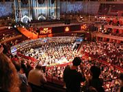 The Proms 2005. Most people sit, while Promenaders stand in front of the orchestra. The Royal Albert Hall Organ is in the background.
