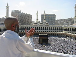 A supplicating pilgrim at Masjid Al Haram, the mosque which was built around the Ka`aba (the building at center).  Thousands of pilgrims walk around the Kaaba in a counter-clockwise direction.