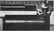 Cylinder on Dictaphone dictation machine. The recording head moved R-L.  The black lines are shiny gaps between tracks.  Wax cylinders could record 1200-1500 words.  They could be reused 100-120 times by putting them in a machine that erased them by 'shaving' off the surface.