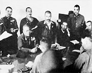 Lieutenant-General Yamashita (seated, centre) thumps the table with his fist to emphasise his demand for unconditional surrender. Lieutenant-General Percival sits between his officers, his clenched hand to his mouth. (Photo from Imperial War Museum).