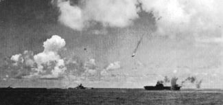 A Japanese Val dive bomber (center) is shot down during the attack on the Enterprise (lower right).  Enterprise is smoking from earlier bomb hits as another bomb near-misses the carrier. In the lower middle is the battleship USS South Dakota.