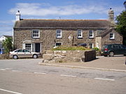 Stone cross in St Buryan village churchtown and Belmont house, former location of the King's Arms public house, in the background