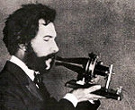 Alexander Graham Bell speaking into prototype model of the telephone