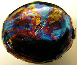 A lump of hafnium which has been oxidized on one side and exhibits thin film optical effects.