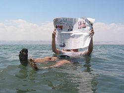 A tourist (on the Jordanian side) demonstrates the unusual buoyancy caused by high salinity.