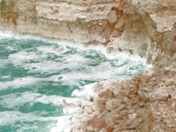 A rough Dead Sea, with salt deposits on cliffs.