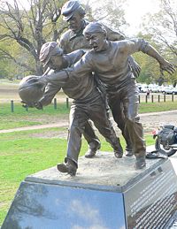 A statue next to the Melbourne Cricket Ground on the approximate site of the 1858 "foot-ball" match between Melbourne Grammar and Scotch College.  Tom Wills is depicted umpiring behind two young players contesting the ball.  The plaque reads: "Wills did more than any other person - as footballer and umpire, co-writer of the rules and promoter of the game - to develop Australian Football during its first decade."