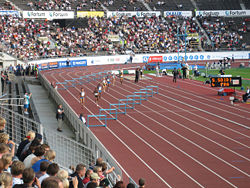 A women's 400 m hurdles race on a typical outdoor red urethane track in the Helsinki Olympic Stadium in Finland.