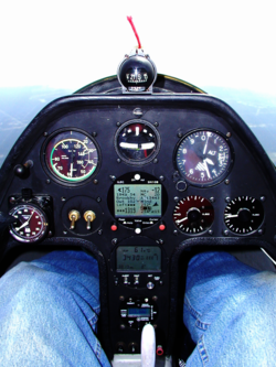 Schempp-Hirth Janus-C in flight, showing instrument panel equipped for "cloud flying," configured in the basic-T, with airspeed, attitude and altitude display across the top row; below a GPS-driven computer, with wind and glide information, drives two electronic variometer displays to the right. The yaw string and compass are above the glare shield