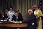 Truman (seated right) and his wife Bess (behind him) attend the signing of the Medicare Bill on July 30, 1965, by President Lyndon B. Johnson.