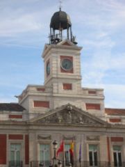 The clock tower at Puerta del Sol, the heart of the city. At the foot of the building lies the Km 0 sign, the center of the Spanish radial road system. Since 1909, the Spaniards traditionally eat twelve grapes on each New Year's midnight at the strikes of this bell.