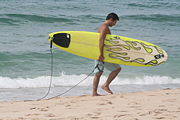 A surfer carries a surfboard along the beach.