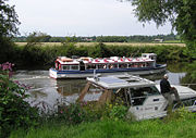 Leisure activities on the River Avon at Avon Valley Country Park, Keynsham, Bristol, England. A boat giving trips to the public passes a moored private boat.