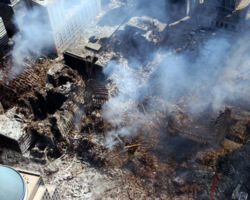 Portions of the outer shells of the South Tower at right and the North Tower at center left, as well as damage to all the other buildings at the WTC site are shown